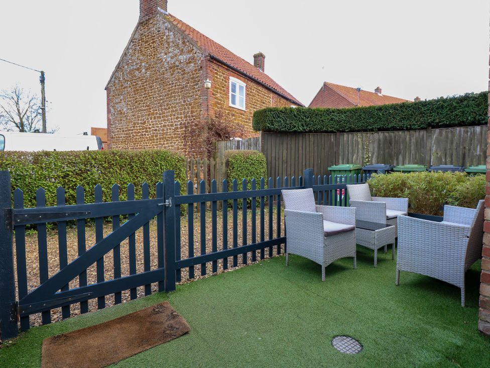 An outdoor patio area with four wicker chairs and a small table on artificial grass near a blue wooden gate at Herbies Cottage in Snettisham