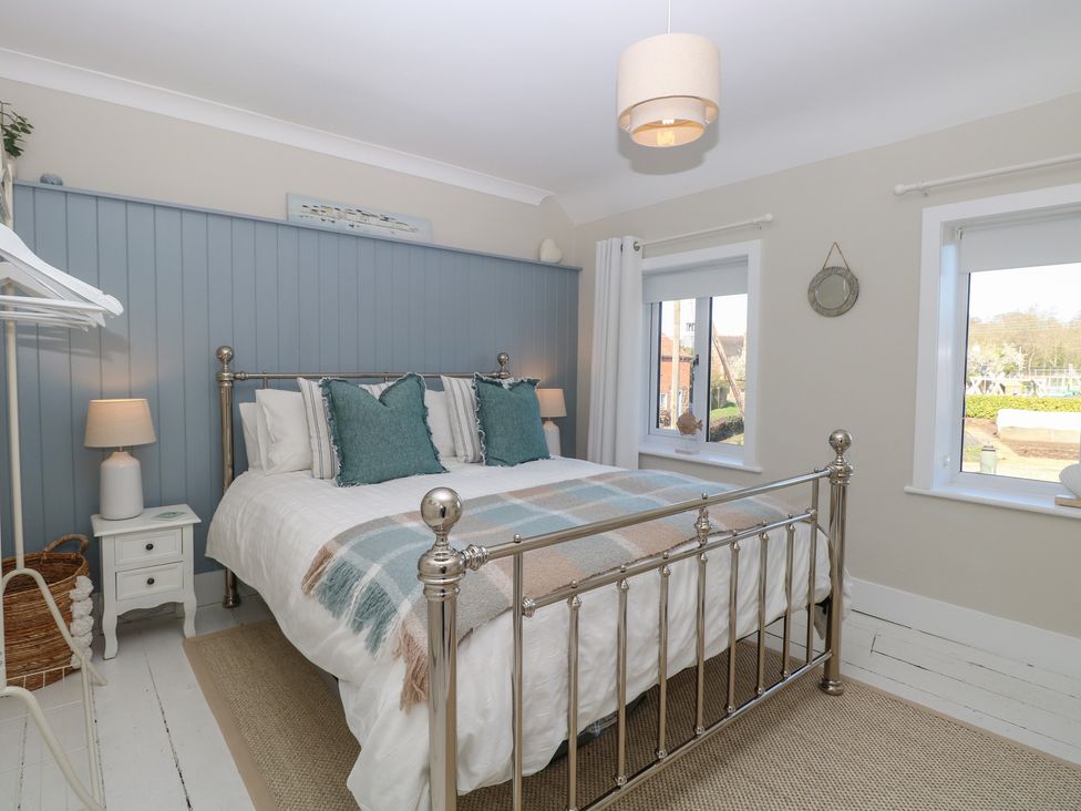 A bedroom with a bed and windows at Herbies Cottage Snettisham