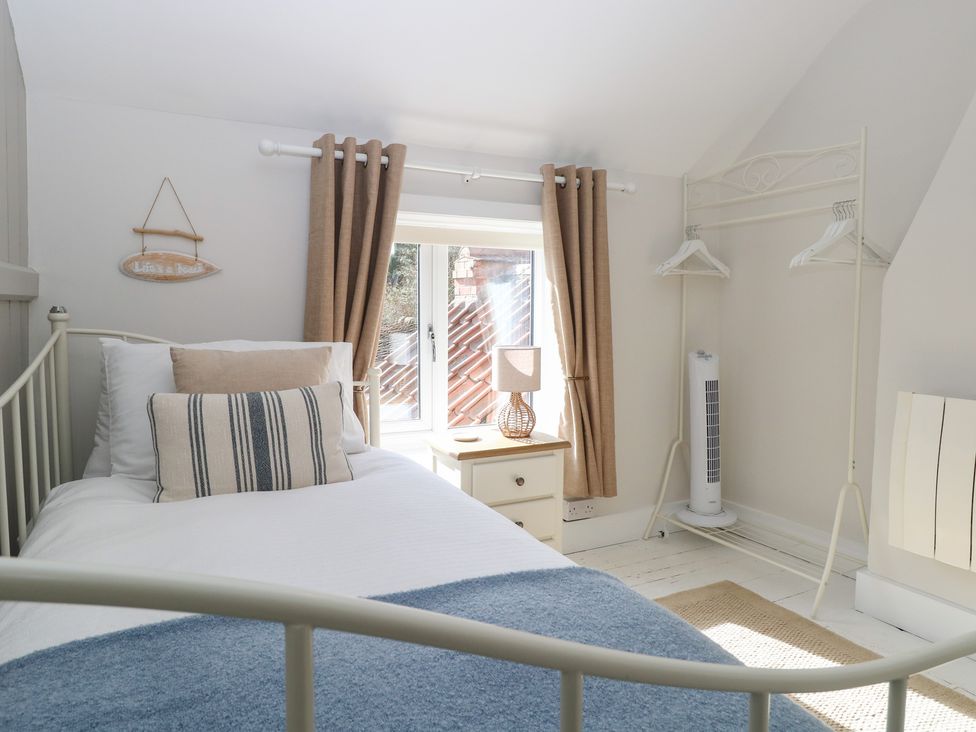 A bedroom with a bed, nightstand, and window at Herbies Cottage in Snettisham