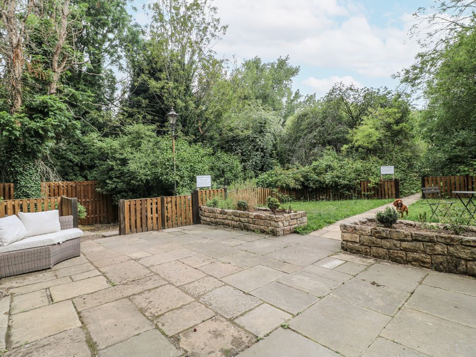 A garden with a sofa, stone wall, and dog at Cotton Mill Cottage in Cuckney