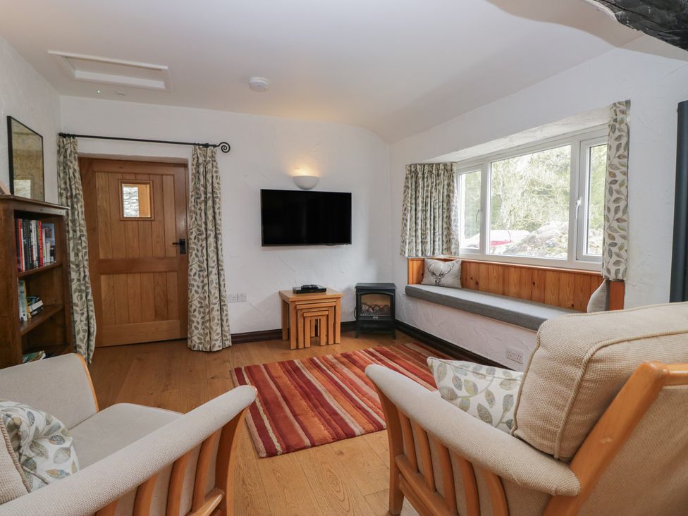 A living room with a television and bookshelf at Woodloft Cottage Elterwater near Chapel Stile