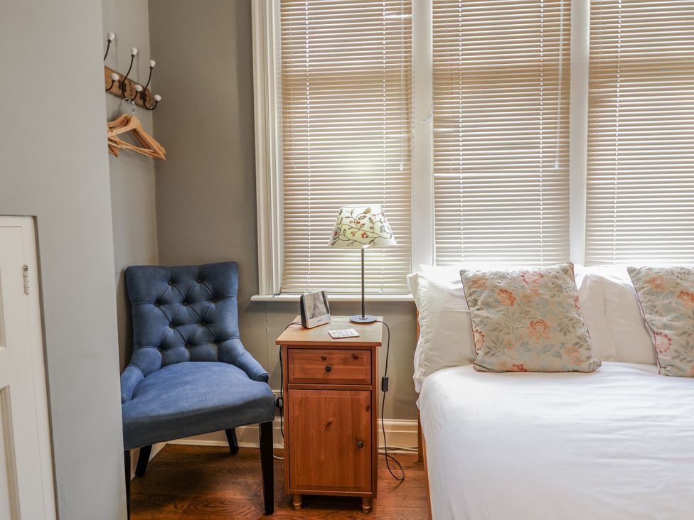 A bedroom with a chair, nightstand, lamp, and bed at Holly Lodge in Aldeburgh