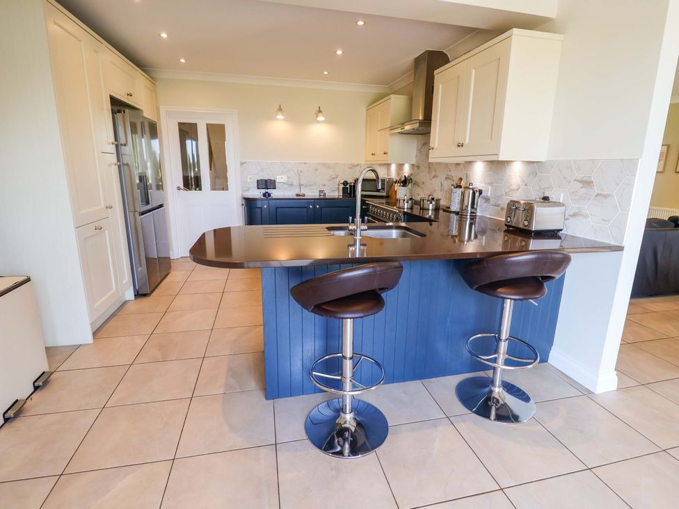 A kitchen with a countertop, sink, and bar stools at Seadrift in Dunwich Near Westleton