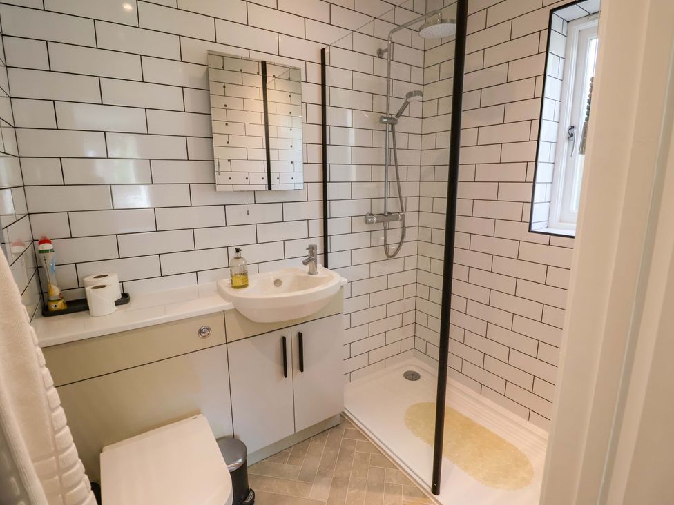 A bathroom with a shower, sink, toilet and mirror at Seadrift in Dunwich Near Westleton