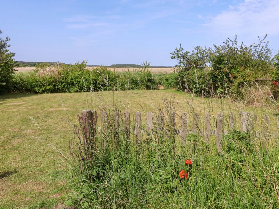 A garden with grass and a wooden fence at Seadrift in Dunwich Near Westleton