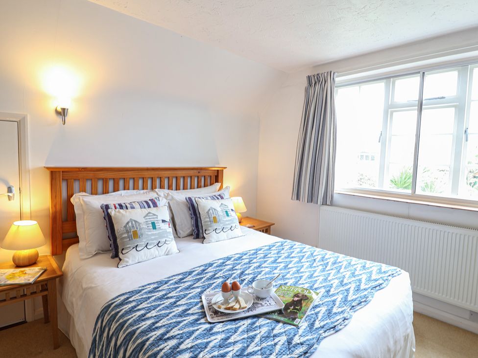 A bedroom with a bed, bedside table, and window at Rippleway, Walberswick