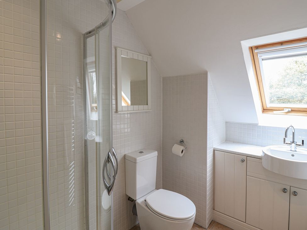 A bathroom with a shower, toilet, mirror, and sink at Rippleway, Walberswick