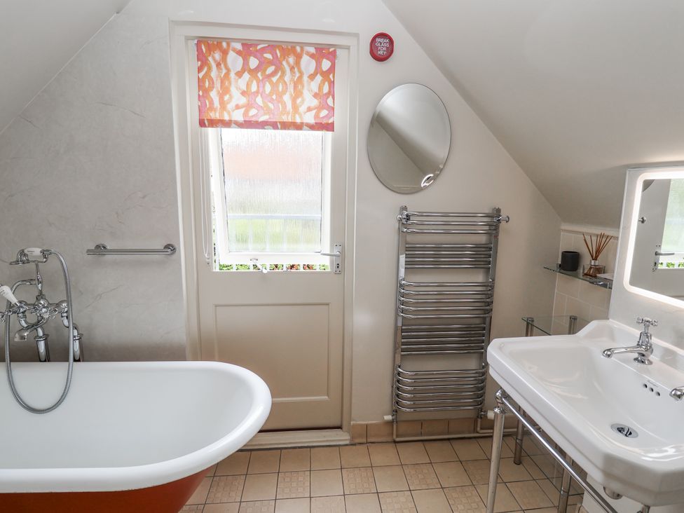 A bathroom with a bathtub, sink, towel rail and mirror at Mariners Cottage, King Street in Aldeburgh
