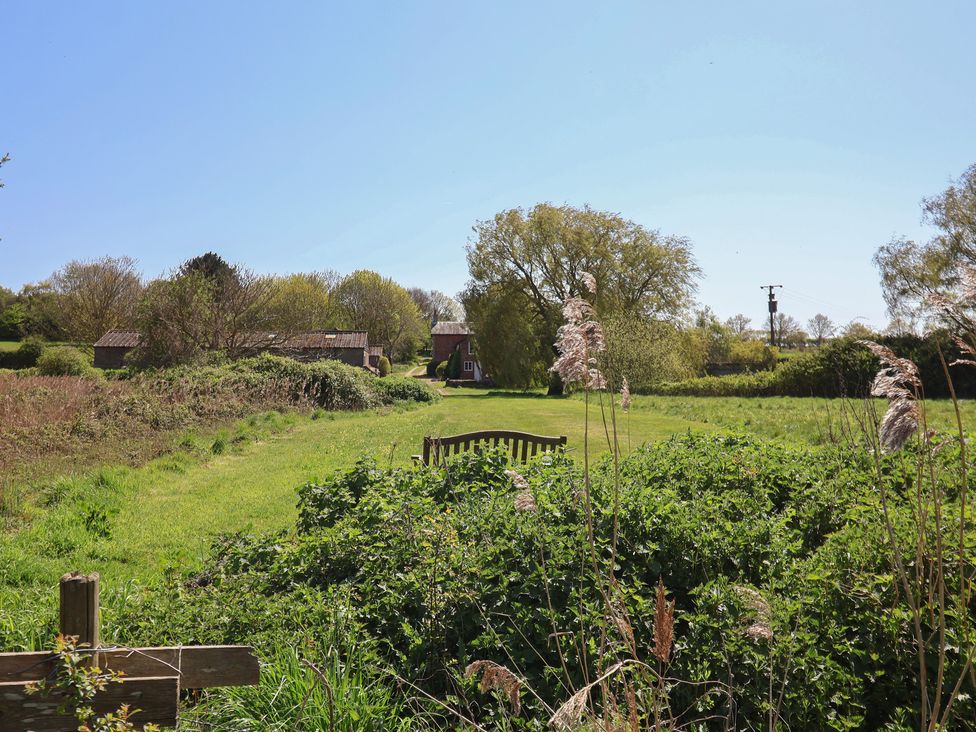 A field with a bench and trees in the background at The Cart House Sudbourne Near Orford
