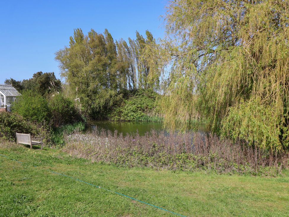 A pond with a bench and trees at The Cart House Sudbourne Near Orford