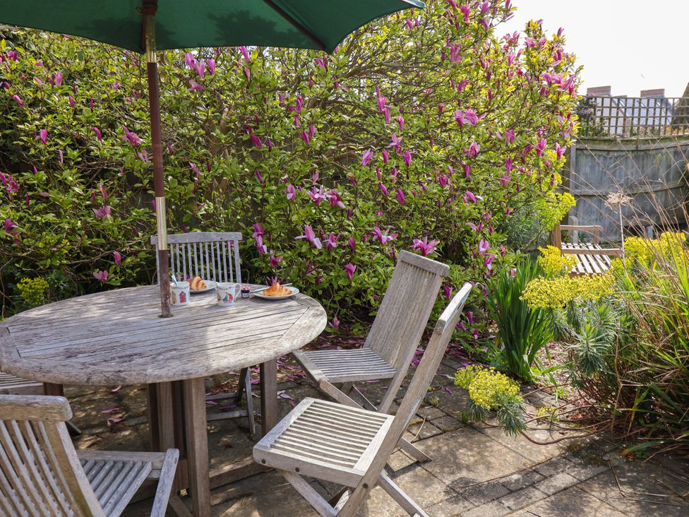 A garden with a wooden table and chairs surrounded by flowering plants at Robert Sadler's Studio, Aldeburgh