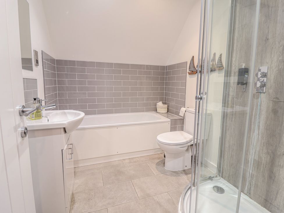 A bathroom with a sink, bathtub, toilet, and shower at Corner Cottage, Thorpeness