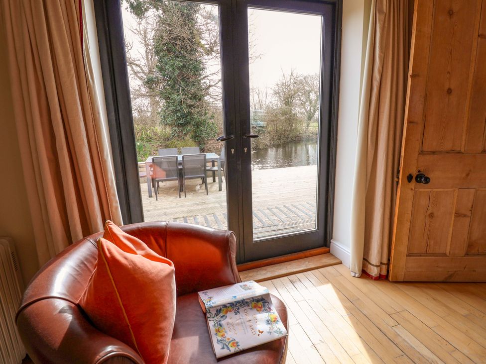 A living room with an armchair and a view of decking outside at Fishpond House, Sotherton