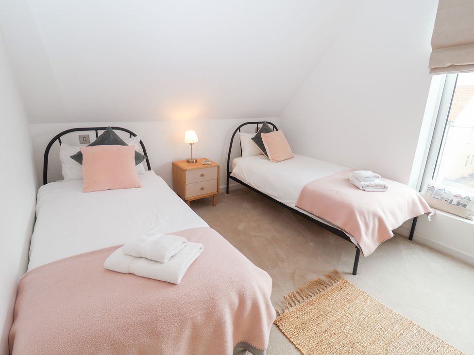 A bedroom with two beds, a nightstand, and a window at Salt Marsh House, Southwold