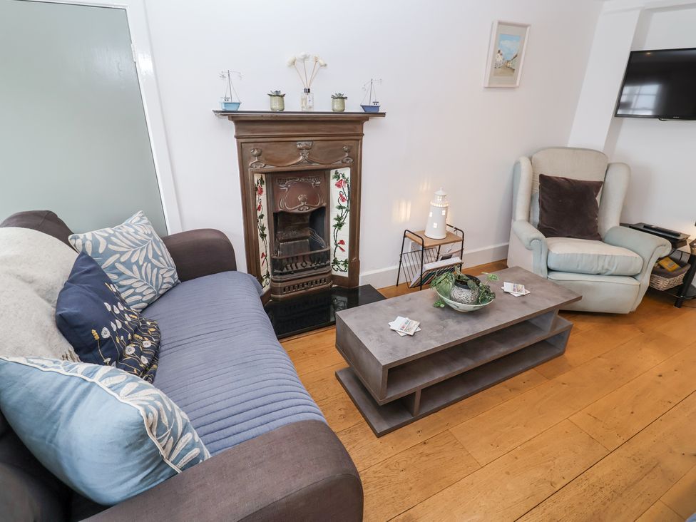 A living room with a sofa, armchair, coffee table, fireplace and wall-mounted TV at Dolphin Cottage Southwold