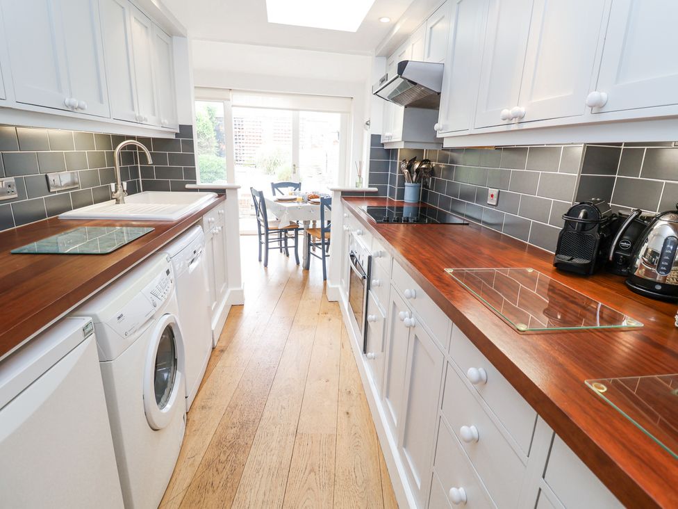 A kitchen with wooden countertops white cabinets and appliances leading to a dining area at Dolphin Cottage Southwold