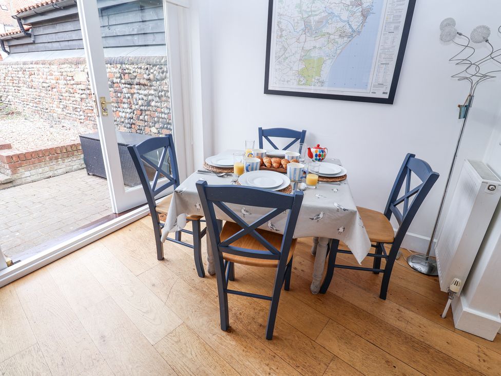 A dining area with a wooden table and four blue chairs set with plates mugs orange juice and croissants by a glass door with a map on the wall at Dolphin Cottage Southwold