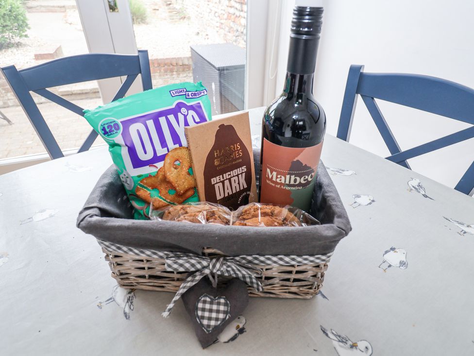 A basket with a bottle of Malbec wine a chocolate bar pretzels and cookies on a table with seagull patterned tablecloth at Dolphin Cottage Southwold