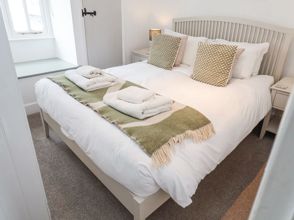 A bedroom with a bed with white linens and green patterned pillows and folded towels on a green runner at Dolphin Cottage Southwold