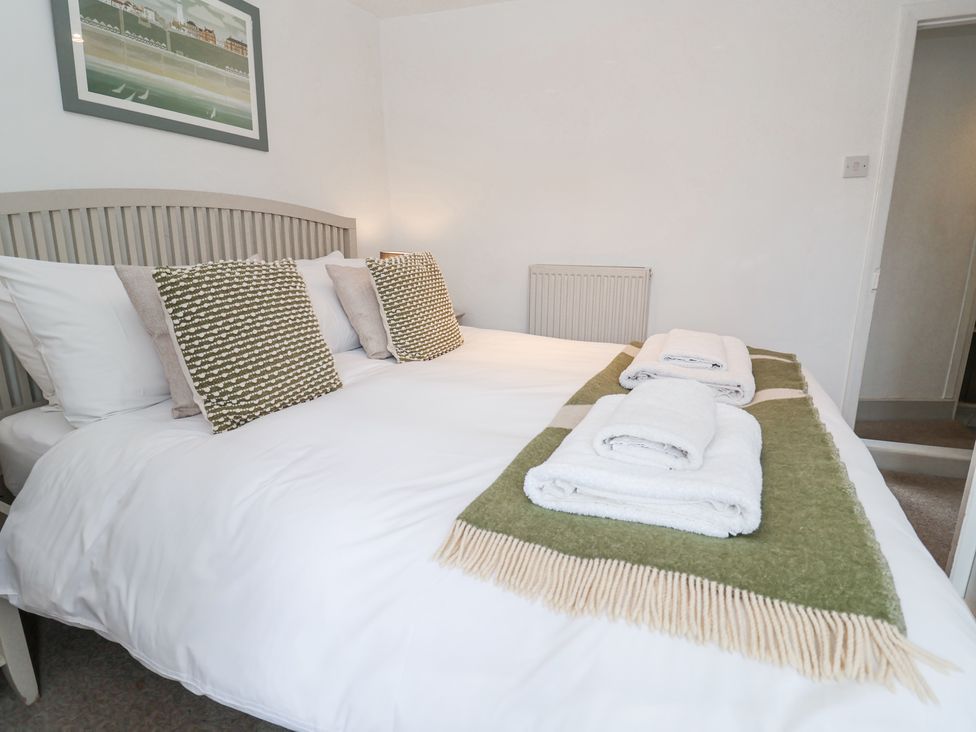 A bedroom with a bed made with white linens and patterned pillows a green and beige throw and folded towels on the bed at Dolphin Cottage Southwold