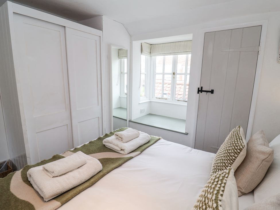 A bedroom with a bed with folded towels on it a window seat a white wardrobe and a closed door at Dolphin Cottage Southwold