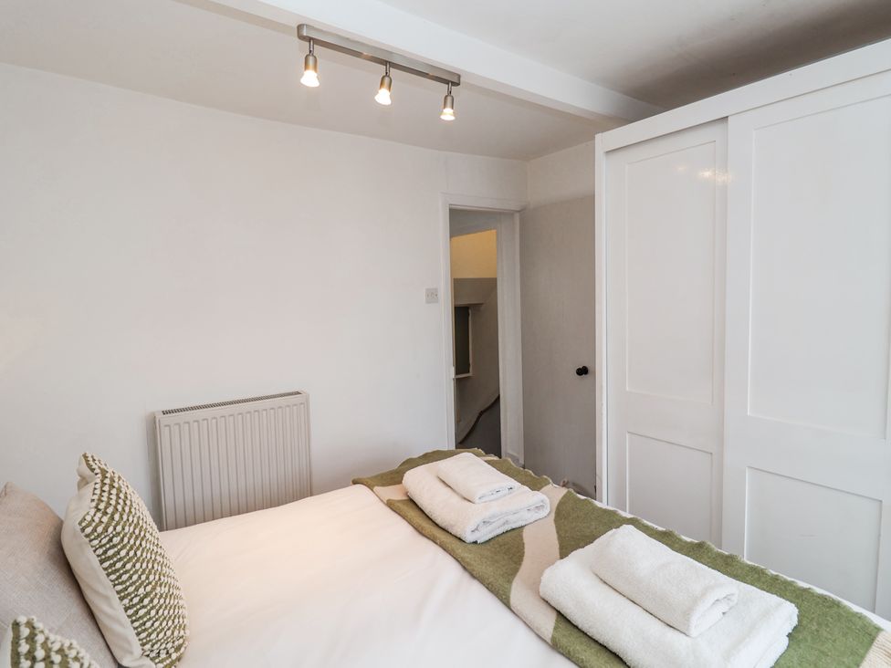 A bedroom with a bed with folded towels and pillows beside a white sliding door wardrobe at Dolphin Cottage Southwold