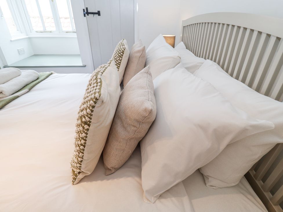A bedroom with a bed made with pillows and folded towels next to a window at Dolphin Cottage Southwold