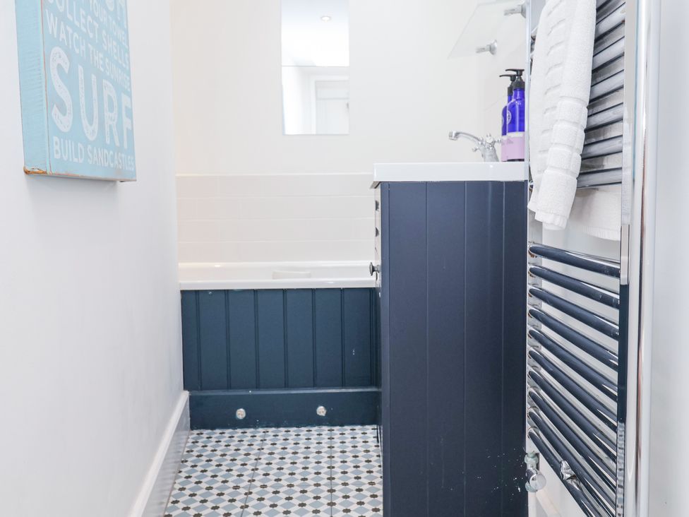 A bathroom with a bathtub a sink cabinet a mirror a towel rack with towels and a wall decoration at Dolphin Cottage Southwold