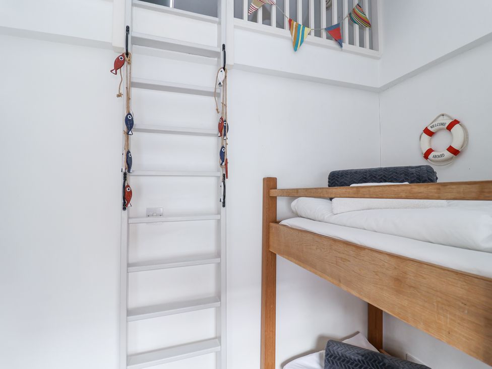 A wooden bunk bed with folded blankets and a white ladder decorated with small fish ornaments in a white room at Dolphin Cottage Southwold
