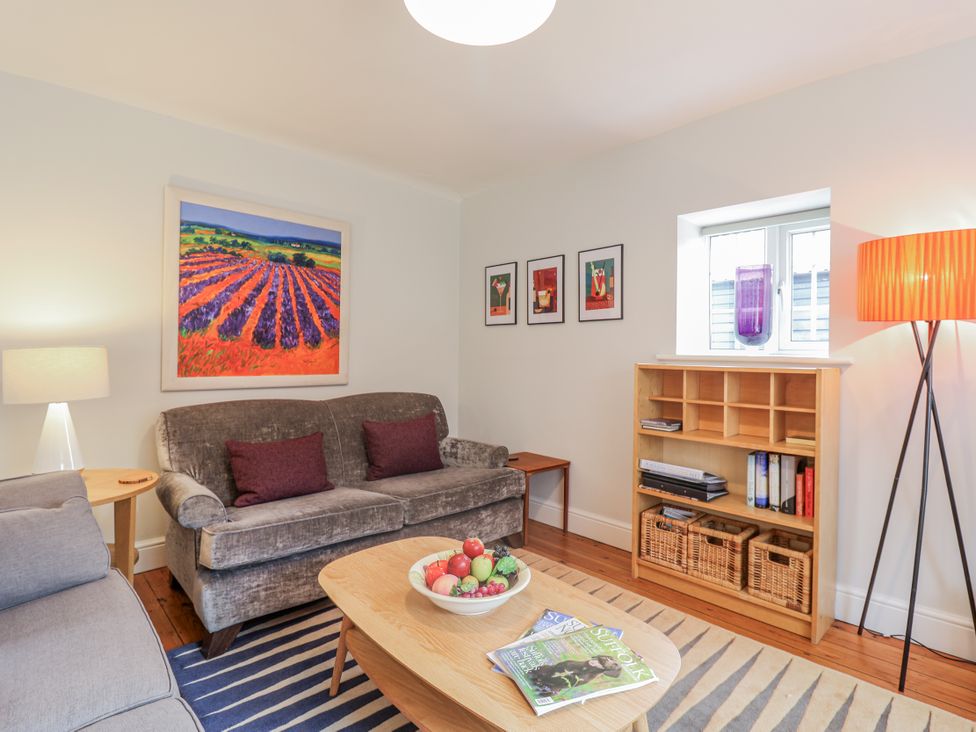A living room with a sofa, armchair, and bookshelf at Fig Cottage, Pettistree Near Woodbridge