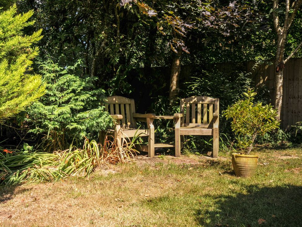 A garden with two wooden chairs and a planter at The Mews in Blisland