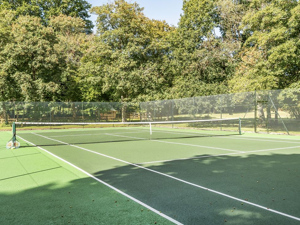 A tennis court with a net and surrounding trees at The Annex in Wimborne Minster