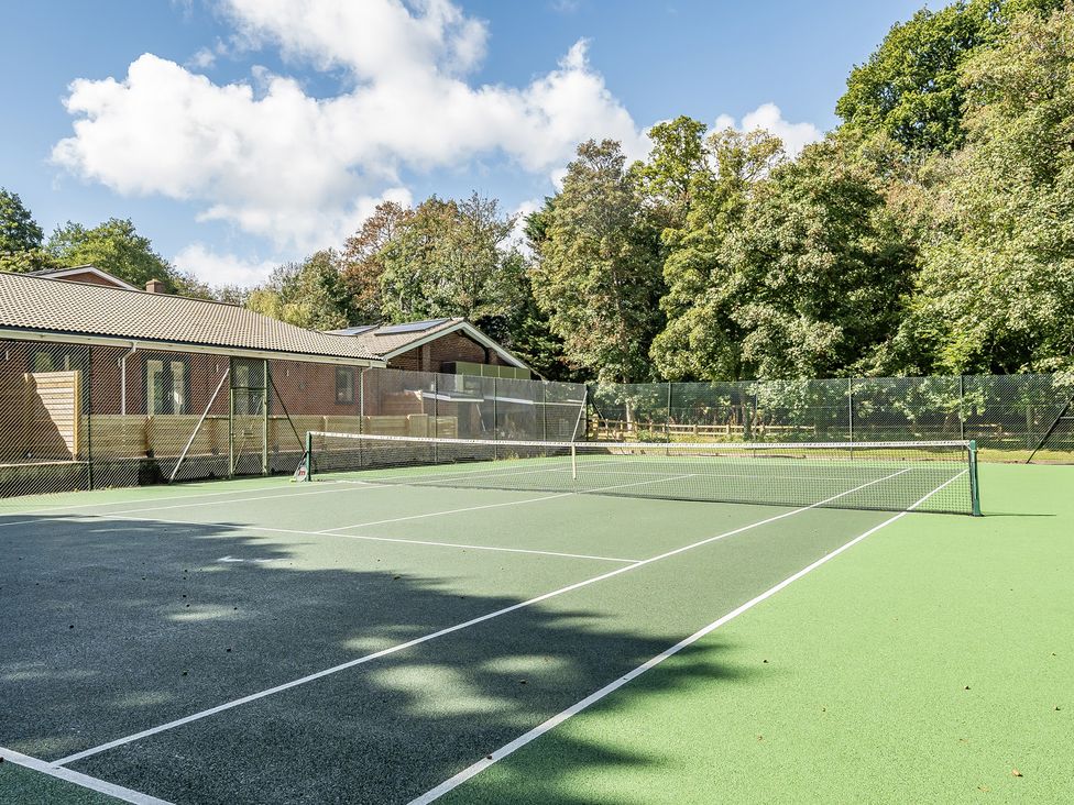 A tennis court with a net and surrounding trees at The Annex in Wimborne Minster