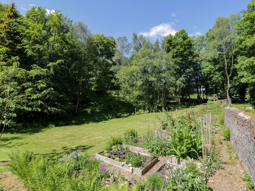 A garden with flower beds and trees at Nithbank Cottage in 