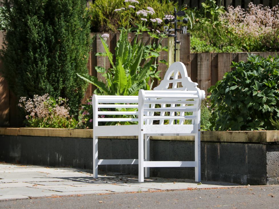 A bench in a garden with plants and flowers at Nithbank Cottage