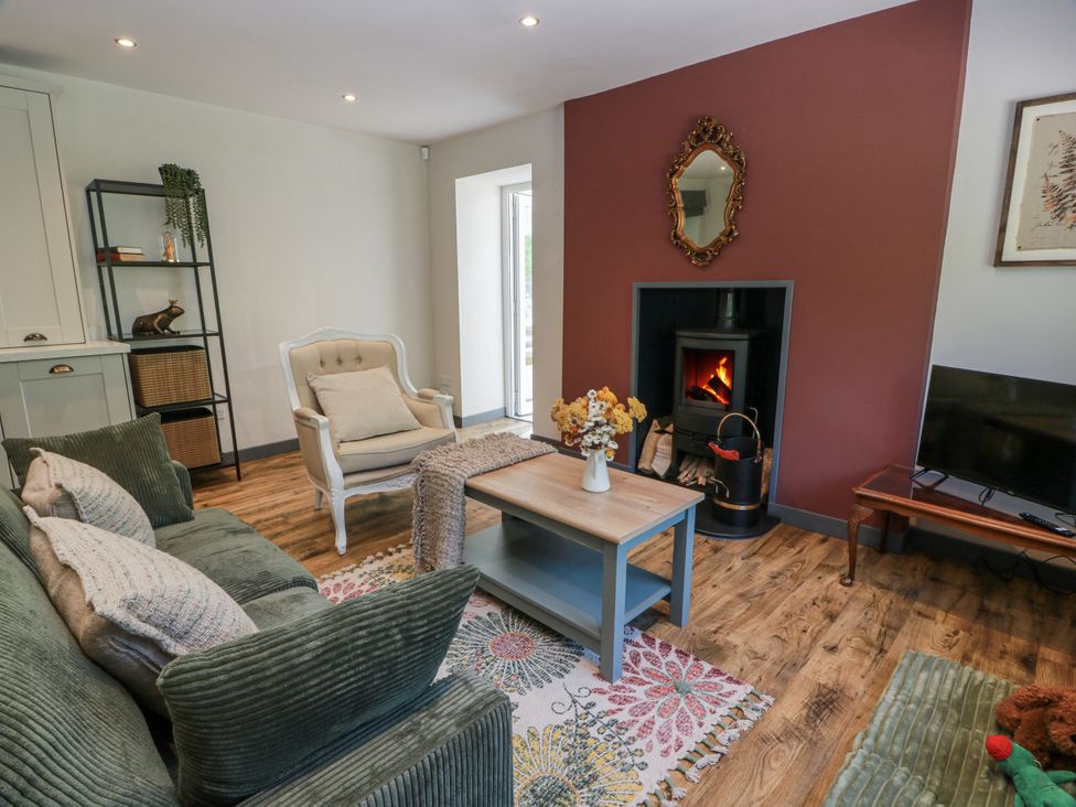 A living room with a sofa, armchair, coffee table, and television at Nithbank Cottage in Thornhill