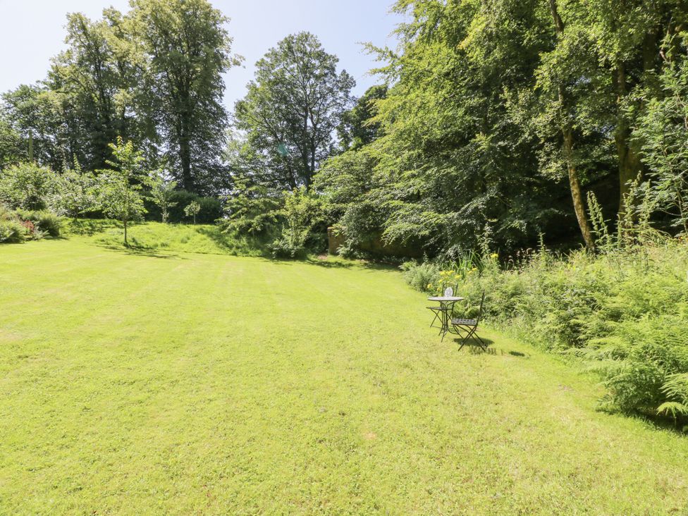 A garden with grass, trees, a table, and a chair at Nithbank Cottage Thornhill