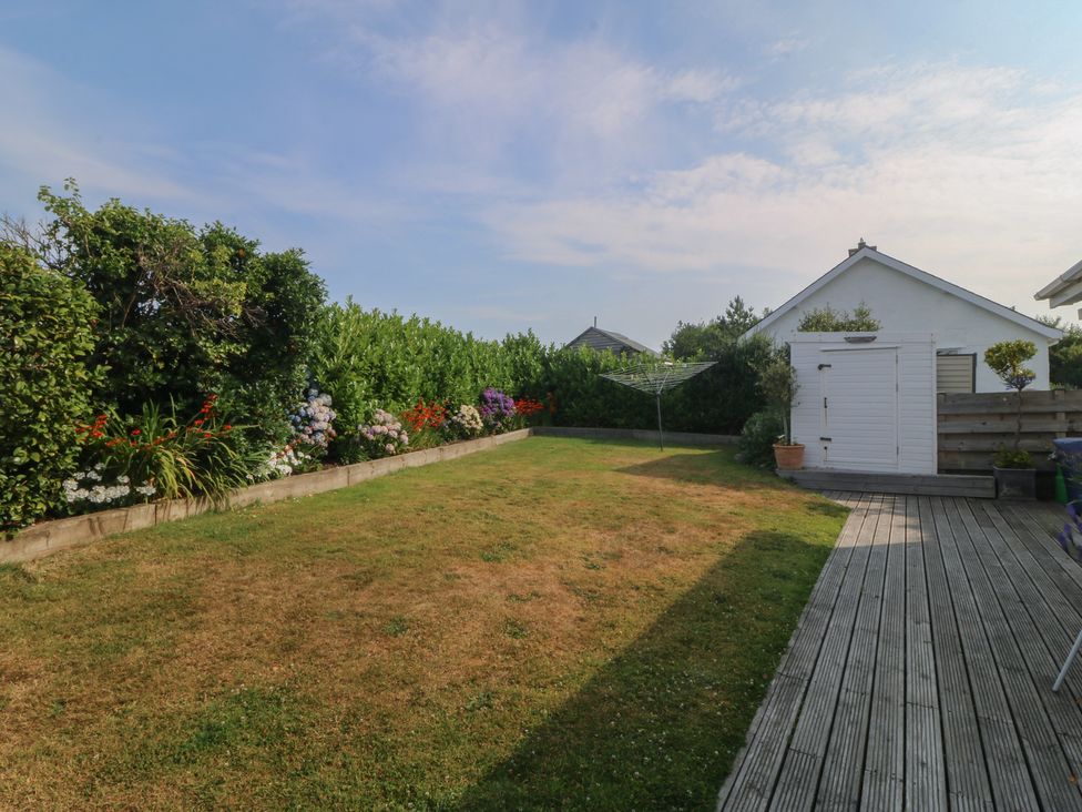 A garden with flower beds and a shed at Trem Ynys in Mynytho near Abersoch