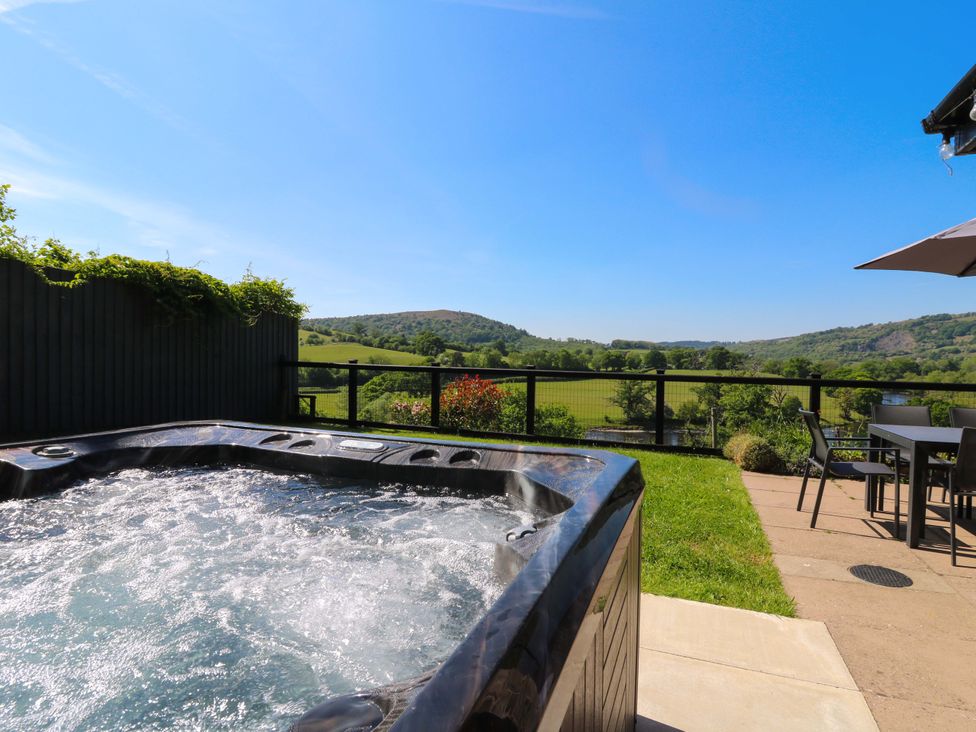 An outdoor patio with a bubbling hot tub table and chairs overlooking green hills and fields at Pen Y Banc in Llanfaredd near Builth Wells