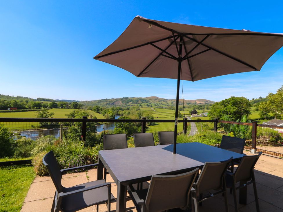 An outdoor patio table with chairs and an umbrella overlooking a river and green hills at Pen Y Banc in Llanfaredd near Builth Wells