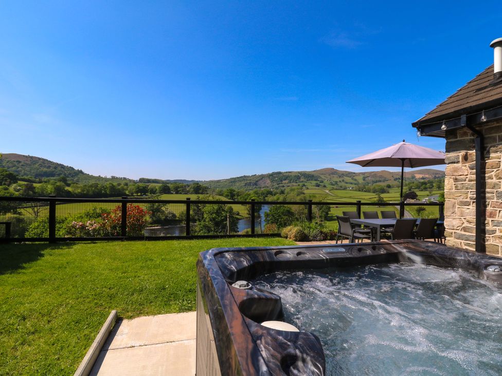 A backyard with a hot tub grass and outdoor dining table with umbrella overlooking hills and a river at Pen Y Banc in Llanfaredd near Builth Wells