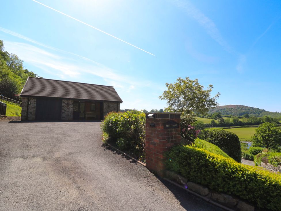 A driveway leading to a stone building with a garage and bench surrounded by greenery at Pen Y Banc in Llanfaredd near Builth Wells