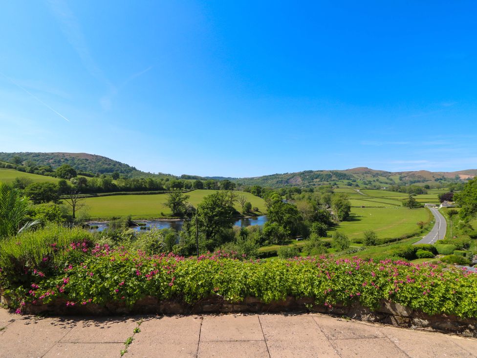 A rural landscape with a road river green fields and hills and a flower bed in the foreground at Pen Y Banc in Llanfaredd near Builth Wells