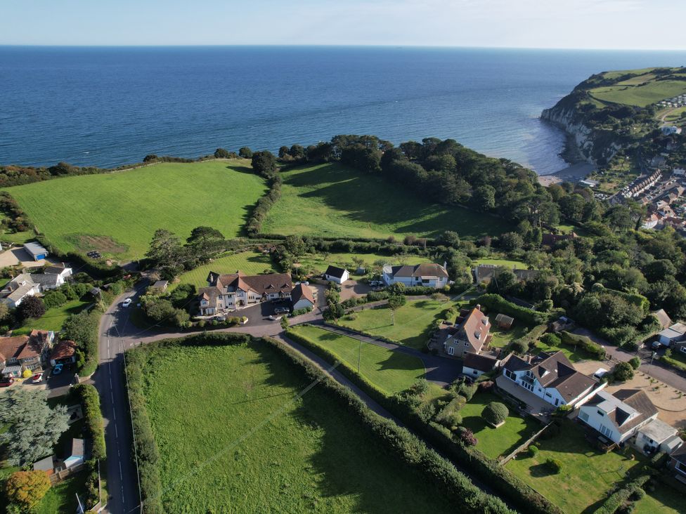 An aerial view of houses with gardens and fields near a coastline with cliffs at The Beach House in Beer