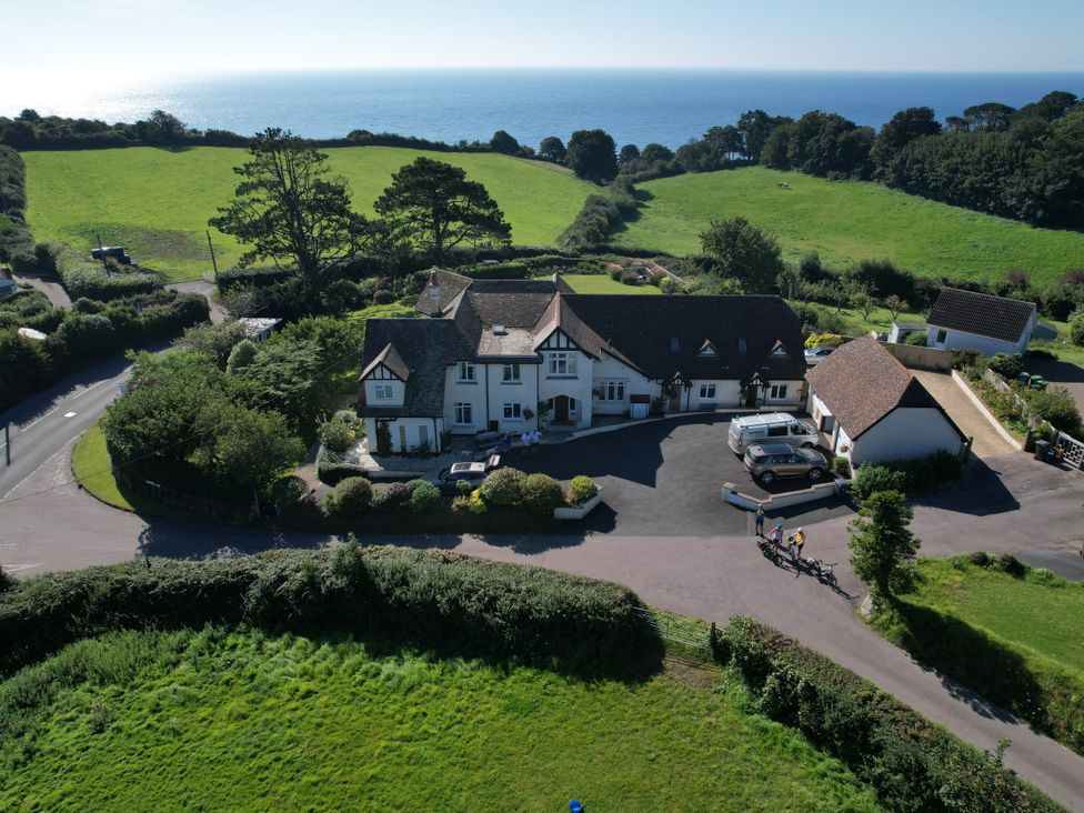 A large house with a courtyard and parked cars surrounded by green fields near the coast at The Beach House in Beer