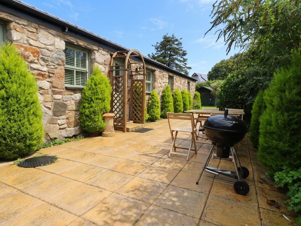 A garden with a stone wall, table, and barbecue at The Old Tannery Beaumaris