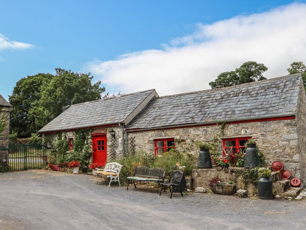 A cottage with a red door, benches, and flower pots at The Dairy in Ardfinnan, County Tipperary