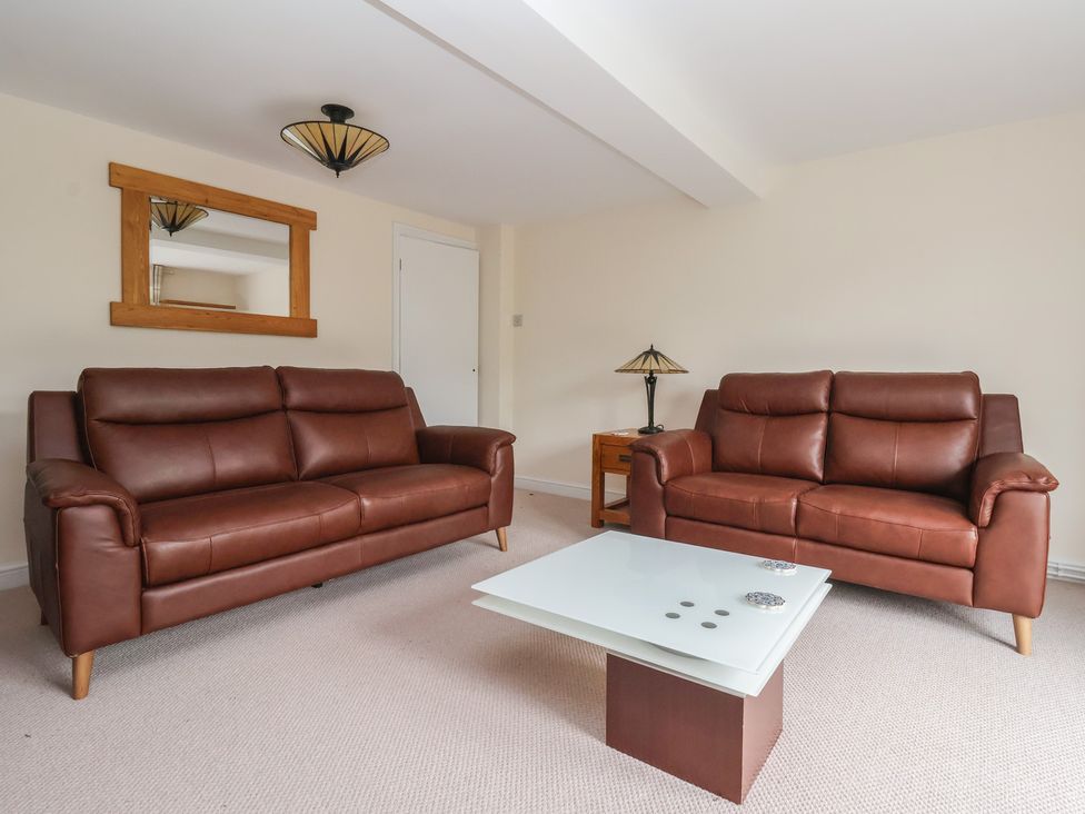 A living room with brown sofas and a glass table at Cliffe House Cottage