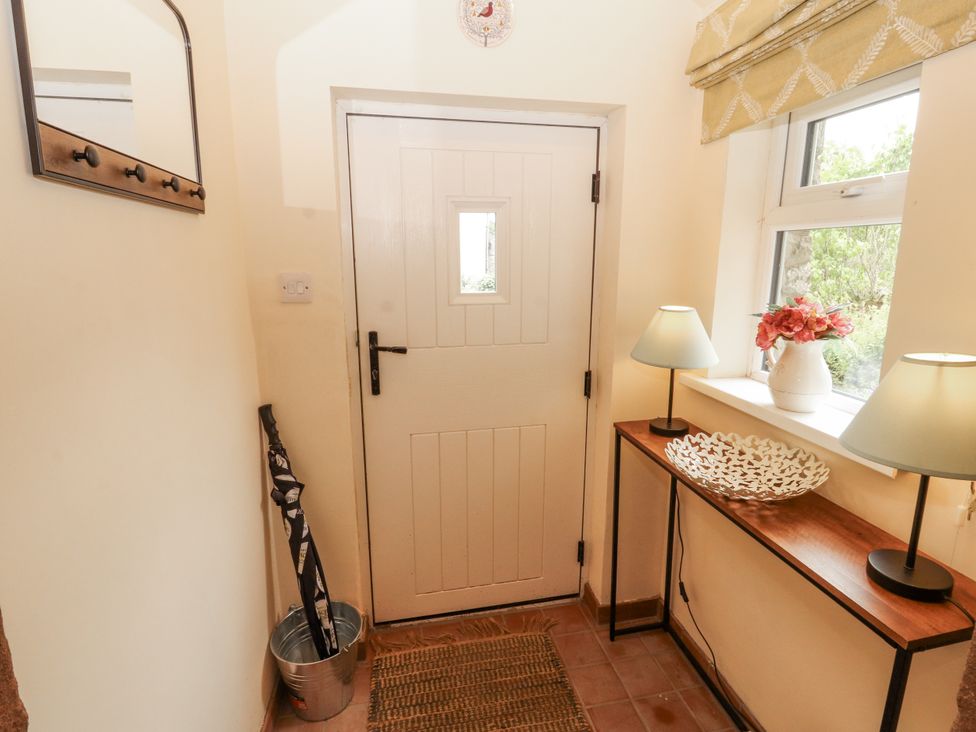 A hallway with a door, table, lamps, and flowers at White House in Shap