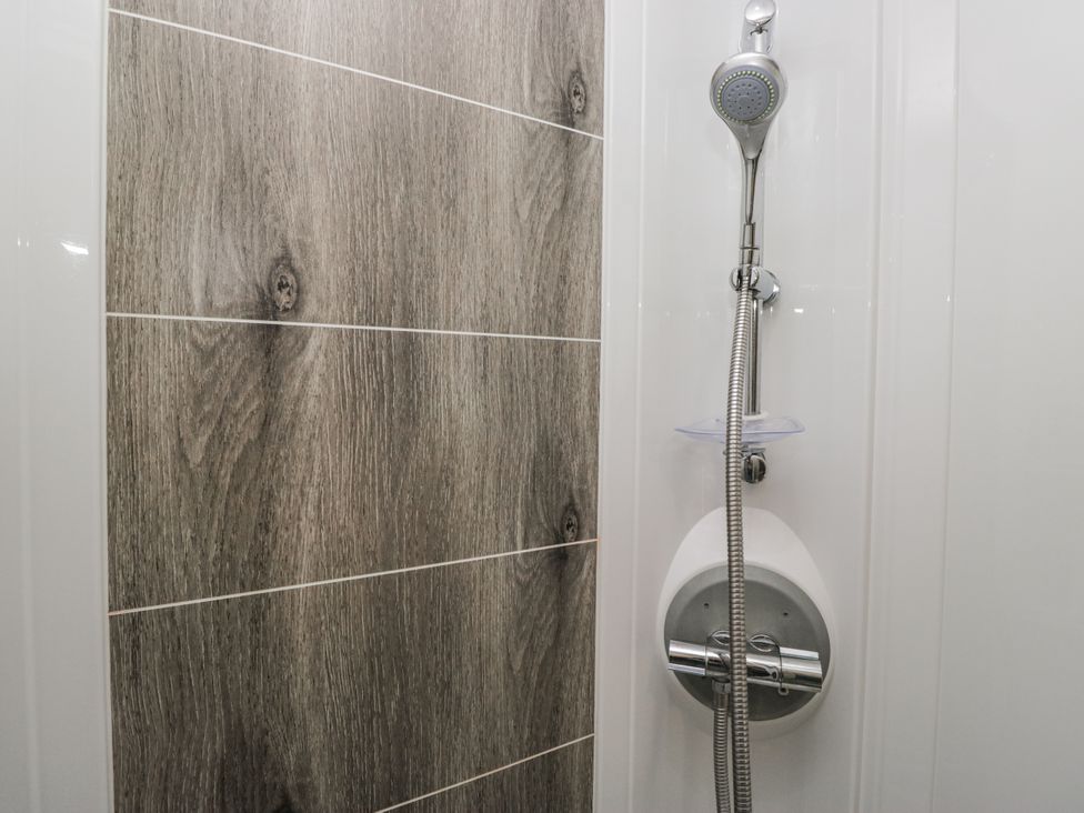 A shower area with a showerhead and tiled wall at Lilac Lodge in Carnforth